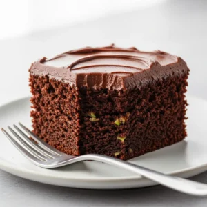 A moist slice of chocolate zucchini cake with rich chocolate frosting on a white plate.
