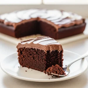 A slice of easy chocolate cake on a white plate, showing the moist crumb and rich chocolate frosting.