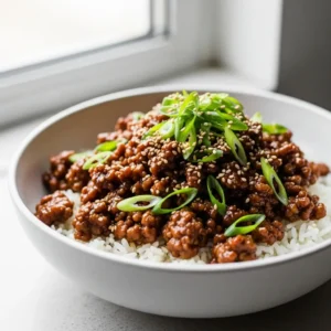 A close-up 45-degree angle shot of a bowl of ground turkey teriyaki served over rice and garnished with green onions.