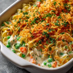 A close-up spoonful of creamy chicken noodle casserole, highlighting the tender shredded chicken, egg noodles, and peas in a rich sauce.