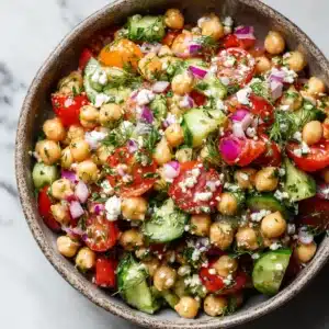 A large rustic bowl filled with a healthy chickpea salad, showcasing the chopped cucumbers, tomatoes, and red onions.