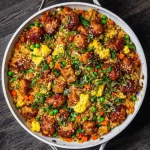 An overhead view of a large skillet filled with creamy chicken fried rice, ready to be served. The rice is mixed with peas, carrots, and egg.