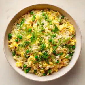 A close-up shot of fluffy egg fried rice in a white bowl, showing separated grains of rice, scrambled egg, peas, and carrots. Highlights the perfect texture of this homemade fried rice.