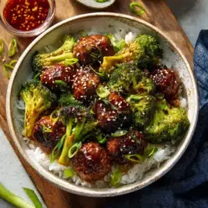 A close-up shot of several Mongolian Meatballs in a skillet, coated in a thick, glossy, sweet and savory sauce.