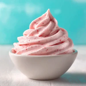 A bowl of freshly whipped strawberry marshmallow fluff frosting with a spatula, showing its smooth and creamy texture before piping.