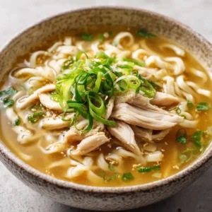 Close-up shot of Ginger Garlic Chicken Noodle Soup showing julienned fresh ginger and drops of toasted sesame oil forming golden pools on the broth.