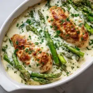 Seasoned chicken breasts and fresh asparagus arranged on a baking sheet before going into the oven.