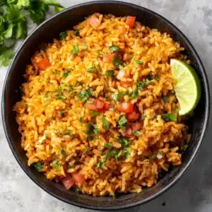 A rustic matte black ceramic bowl filled with fluffy, distinct, reddish-orange tinted long-grain authentic Spanish rice.
