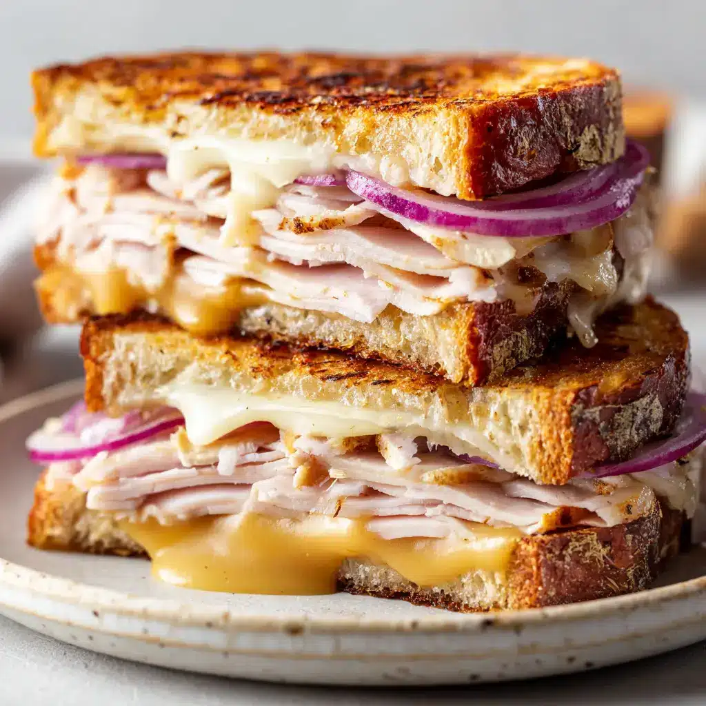 A close-up shot of a halved Turkey Dijon Melt, showing the generous folded layers of juicy deli turkey and crisp red onion.