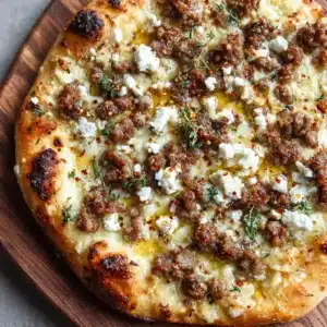 Close up shot of melted mozzarella, browned sausage, and crumbled feta on a golden-brown pizza crust.