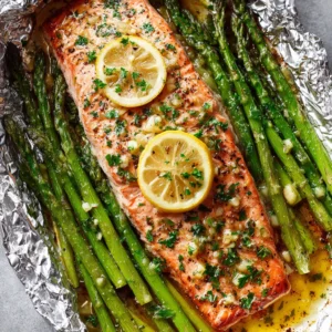 Top-down view of flaky pink salmon with melted garlic butter and lemon slices in foil. (baked salmon in foil)