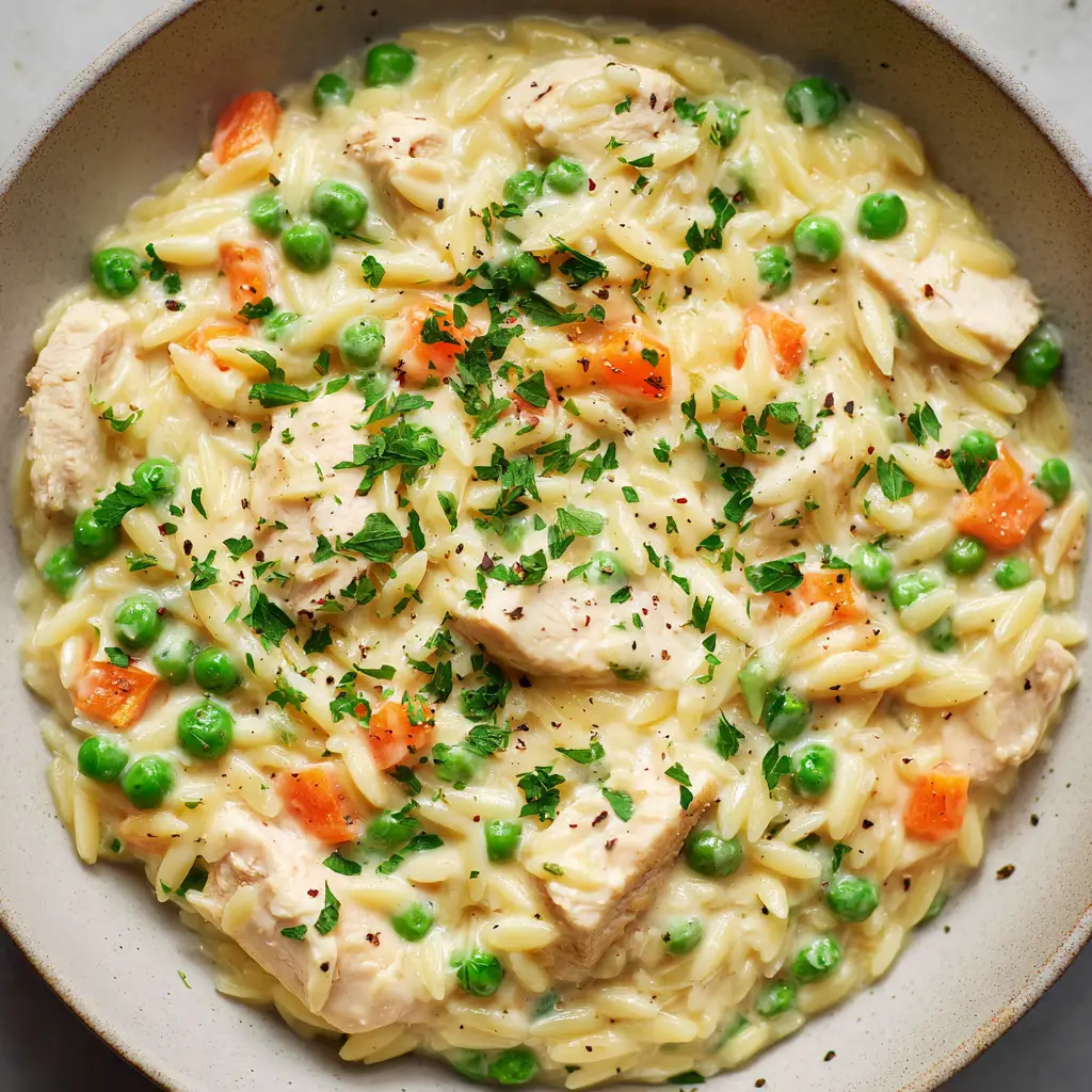 Close-up overhead shot of velvety Chicken Pot Pie Orzo with bright green peas and orange carrots. (Chicken Pot Pie Orzo)