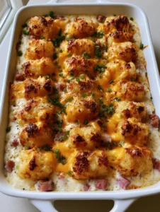 Top-down view of Ham and Tater Tot Casserole in a white dish with rows of charred tots and bubbled orange cheese.